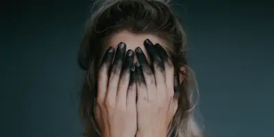 O femeie cu fata acoperita de palme, cu varful degetelor negre