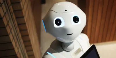 Un robot alb cu ochii mari si o tableta in mana, pe un hol