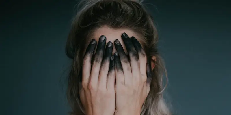 O femeie cu fata acoperita de palme, cu varful degetelor negre